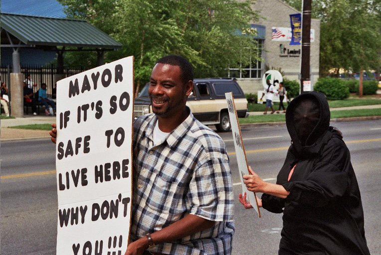 Man holds sign "Mayor, if it's so safe to live here, why don't you?"